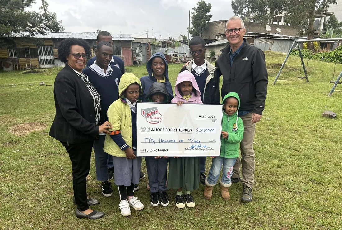 Adults and children outdoors holding an NPSA check made out to AHOPE for Children
